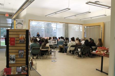 Someone is outside a crowded space and is looking in. A display of books is to the left and in frotn we can see an audience of people.